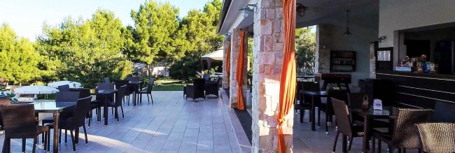 Terrazza esterna con tavoli e sedie vicino a un giardino.