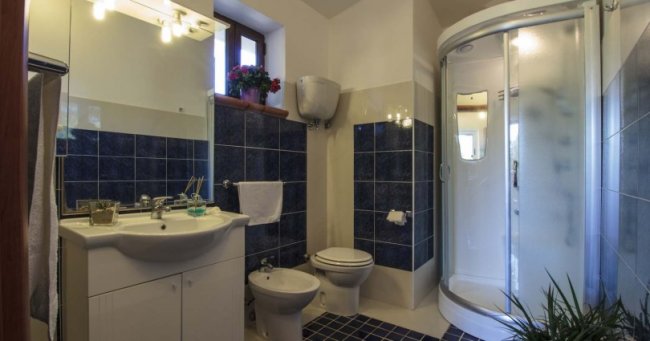 Bagno con piastrelle blu, lavabo, bidet, WC e cabina doccia semicircolare.