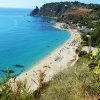 Spiaggia con sabbia dorata, mare azzurro e colline verdeggianti.
