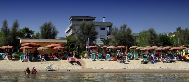 Spiaggia con ombrelloni, sedie a sdraio e persone sul bagnasciuga.