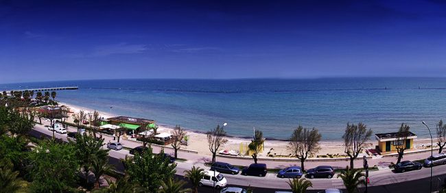 Spiaggia panoramica con strada e auto, mare blu sullo sfondo.
