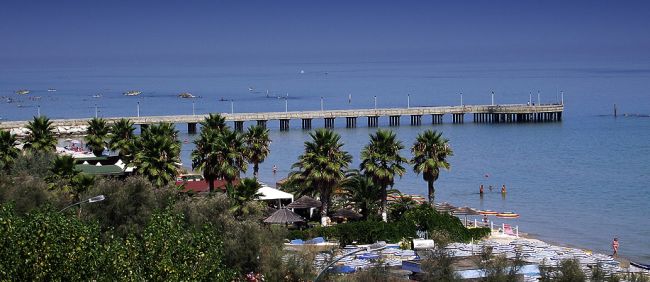 Molo che si estende sul mare, palme lungo la spiaggia.