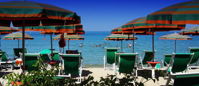 Ombrelloni verdi e arancioni su una spiaggia, persone che nuotano in mare.