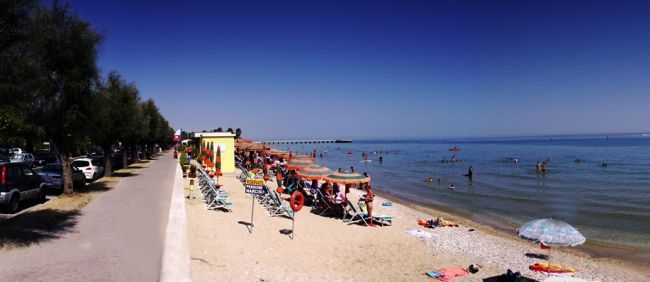 Spiaggia con ombrelloni arancioni, sedie a sdraio e persone che nuotano nel mare.