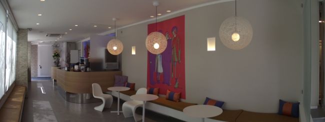 Un moderno caffè con sedie bianche, tavoli rotondi e lampade pendenti.