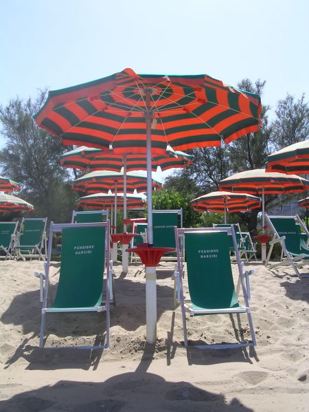 Ombrelloni a righe rosse e verdi con lettini verdi su una spiaggia sabbiosa.