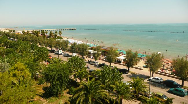 Vista dall'alto di una spiaggia con ombrelloni, strada e auto parcheggiate.