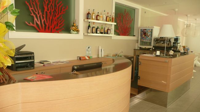 Bancone di un bar con bottiglie sugli scaffali e decorazioni a corallo rosso.