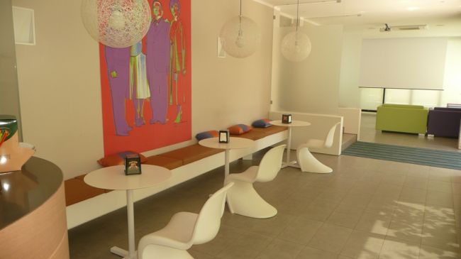 Area salotto moderna con sedie bianche, tavolini e un vivace murale.