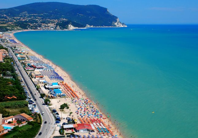 Spiaggia affollata con ombrelloni colorati e mare turchese.
