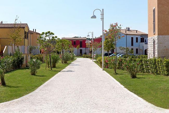 Strada pedonale tra case colorate, alberi e lampioni.