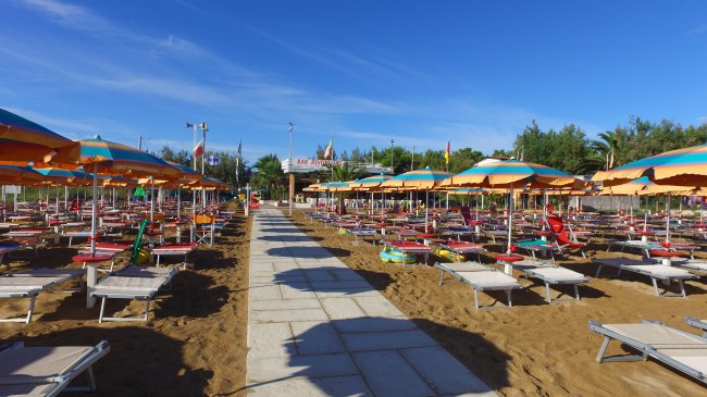 Spiaggia con file di lettini e ombrelloni arancioni e verdi.