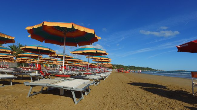 Ombrelloni colorati e lettini allineati su una spiaggia soleggiata.