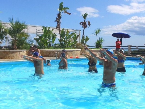 Persone eseguono esercizi in una piscina all'aperto circondata da vegetazione.