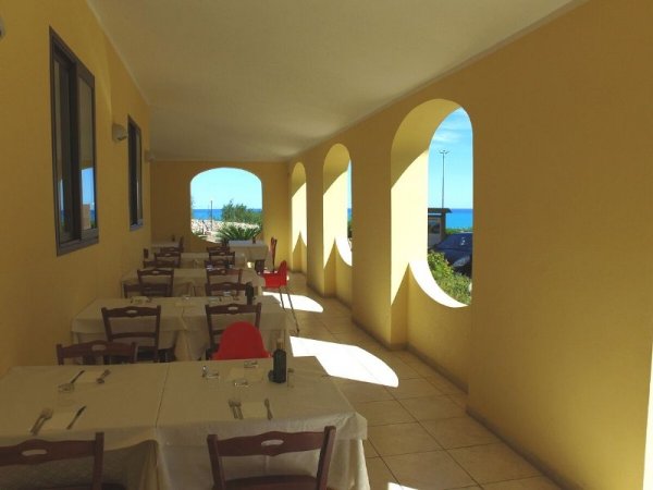 Veranda con tavoli apparecchiati, archi e vista sul mare.