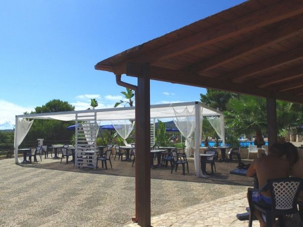 Terrazza con tavoli sotto un gazebo bianco, cielo sereno.