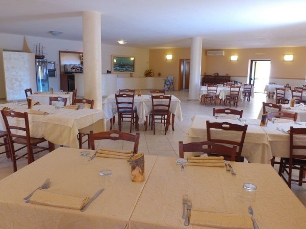 Sala da pranzo con tavoli apparecchiati e sedie di legno in un ambiente luminoso.