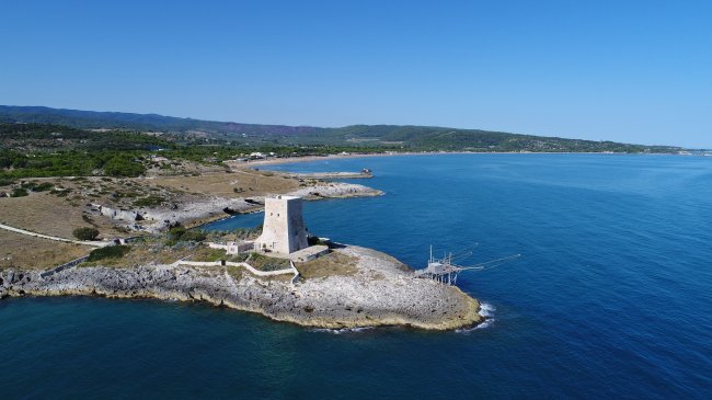 Torre su un promontorio roccioso sul mare, circondata da paesaggio costiero.