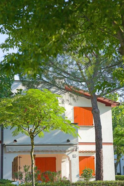 Casa bianca con imposte arancioni tra gli alberi.