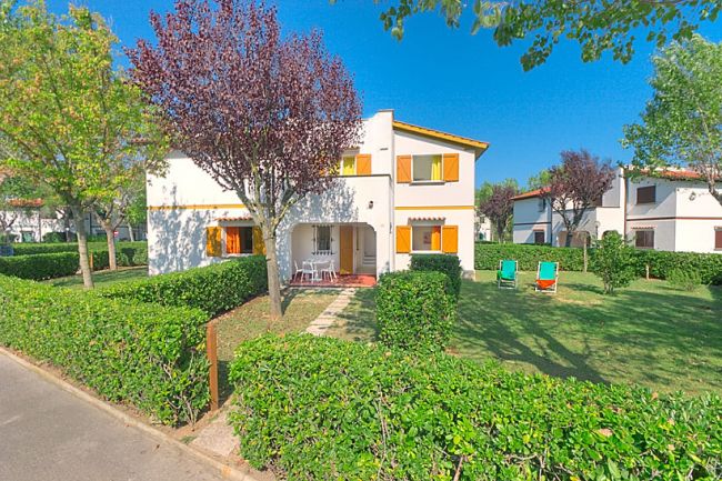 Casa con giardino, sedie e tavolo tra cespugli.