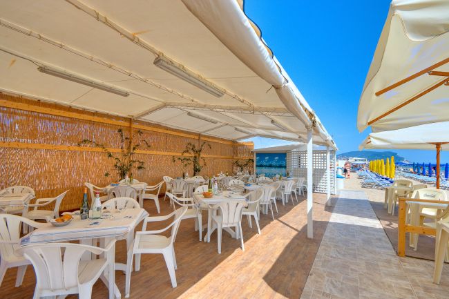 Ristorante all'aperto sulla spiaggia con tavoli e sedie bianche.