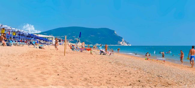 Spiaggia affollata con vista su un promontorio lontano.