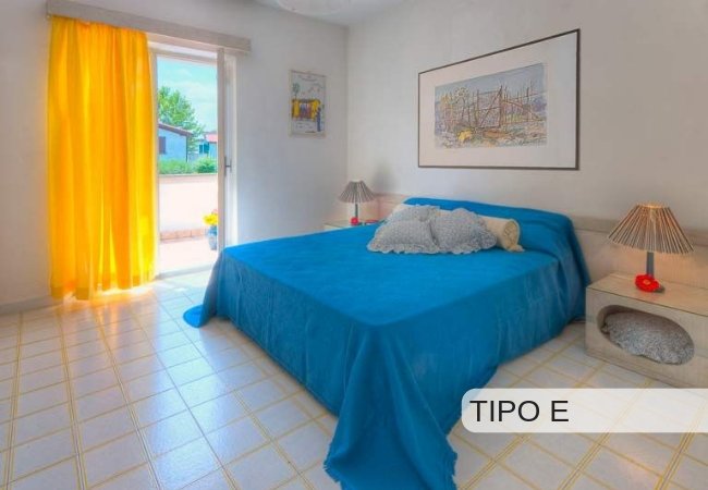 Camera con letto blu, tende gialle e quadro.