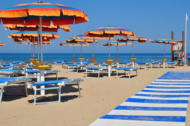 Spiaggia con ombrelloni arancioni e blu, lettini e passerella.