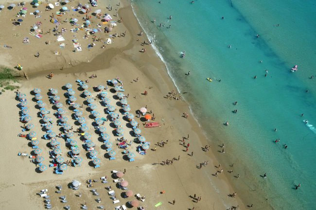 Vista aerea di spiaggia affollata con ombrelloni e mare turchese.