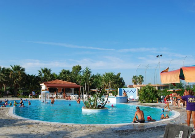Piscina all'aperto con persone e chiosco, cielo sereno.