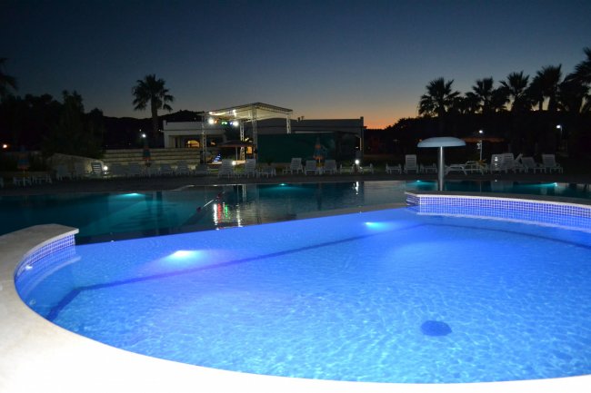 Piscina illuminata al tramonto con palme.