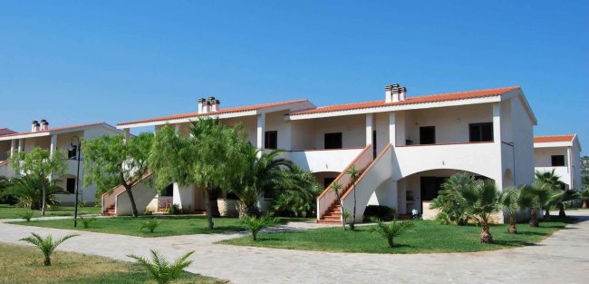 Edifici bianchi a due piani con scale esterne e giardino.