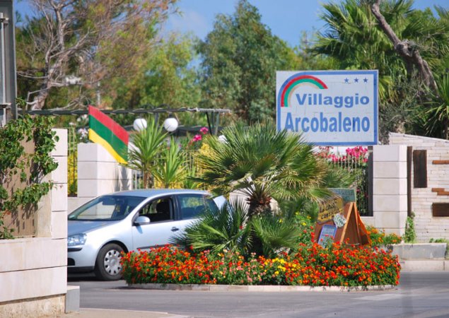 Ingresso di Villaggio Arcobaleno con auto e aiuole fiorite.