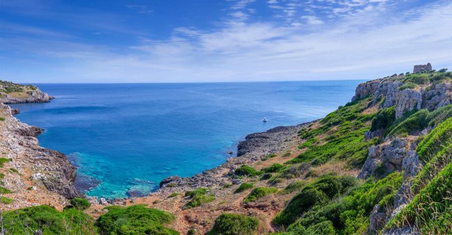 Costa rocciosa con mare blu e cielo sereno.