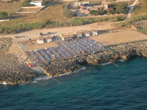 Spiaggia rocciosa con lettini e ombrelloni, vista aerea.