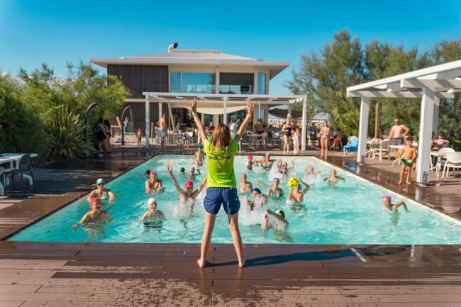 Un istruttore anima un gruppo di persone in piscina durante un'attività di acquagym all'aperto.
