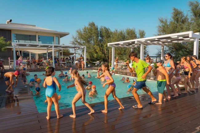 Bambini e adulti corrono lungo il bordo di una piscina durante un'attività di gruppo.