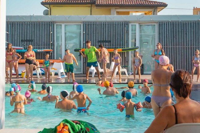 Attività di gruppo in una piscina all'aperto con molti bambini e alcuni adulti.