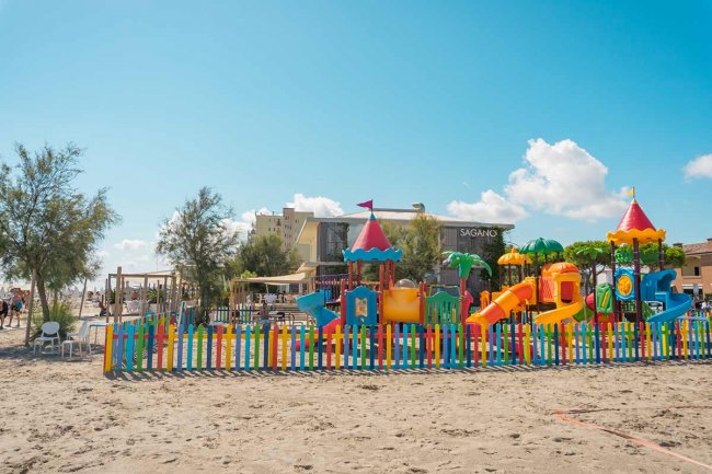 Parco giochi colorato su una spiaggia sabbiosa, circondato da una recinzione.