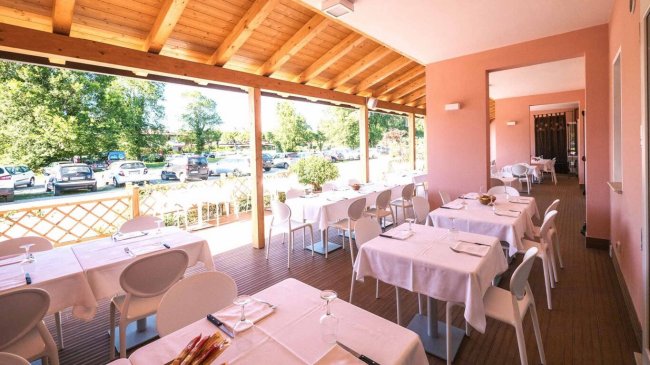 Ristorante all'aperto con tavoli apparecchiati, tetto in legno e vista su un parcheggio alberato.