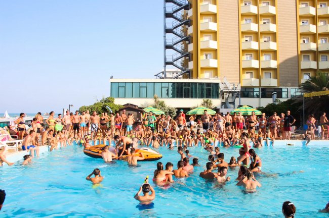 Persone in piscina affollata vicino a un hotel.
