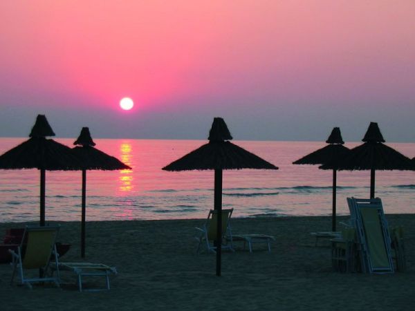 Tramonto su spiaggia con ombrelloni sagomati.