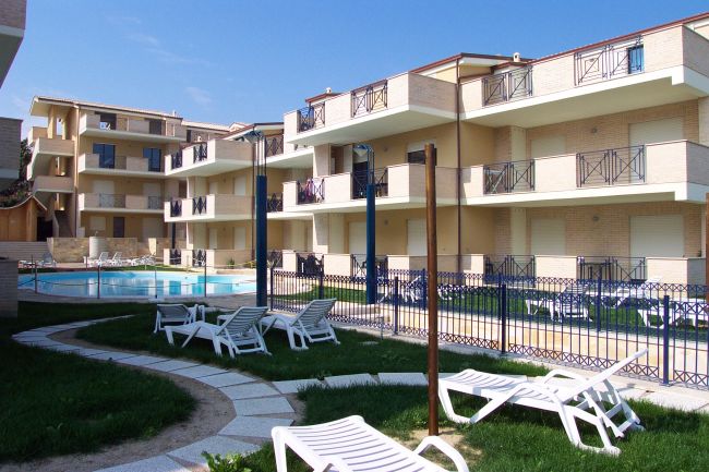 Complesso residenziale con piscina e sedie a sdraio.