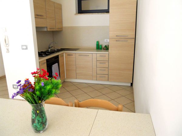 Cucina moderna con mobili in legno chiaro e fiori sul tavolo.