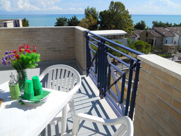 Balcone con tavolo apparecchiato, vista mare e alberi.