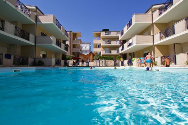 Complesso residenziale con piscina centrale, persone in acqua.