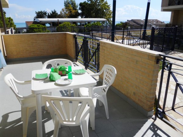 Tavolo bianco con sedie su terrazza soleggiata.