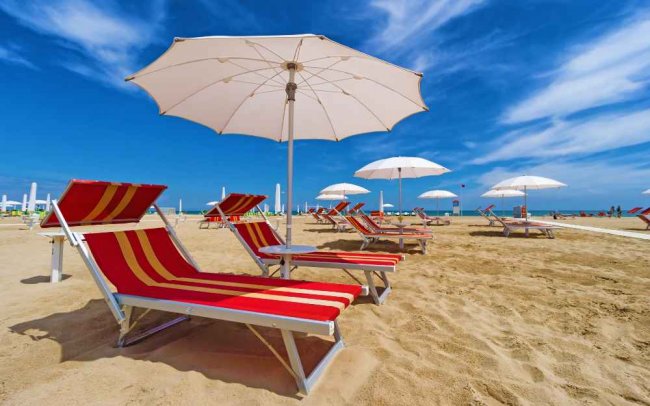 Spiaggia con lettini rossi e ombrelloni bianchi.