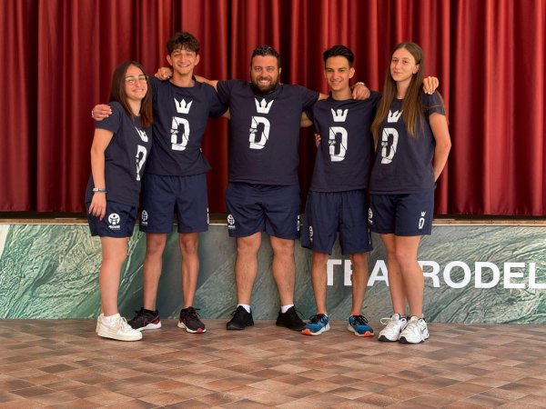 Cinque persone in magliette blu posano sorridenti davanti a una tenda rossa.