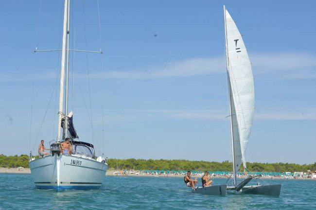 Due barche a vela in mare, spiaggia nello sfondo.